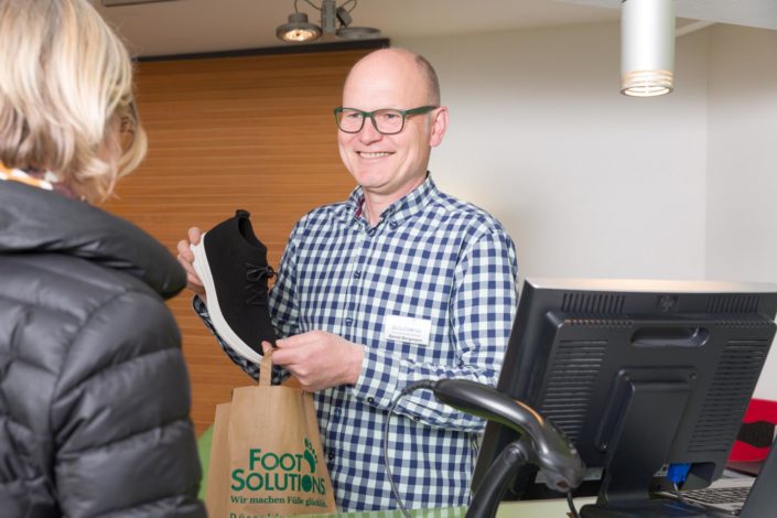 Geschäftsführer Bernd Borgmann packt die gekauften schwarzen Aktivschuhe in die Papiertüte von Foot Solutions
